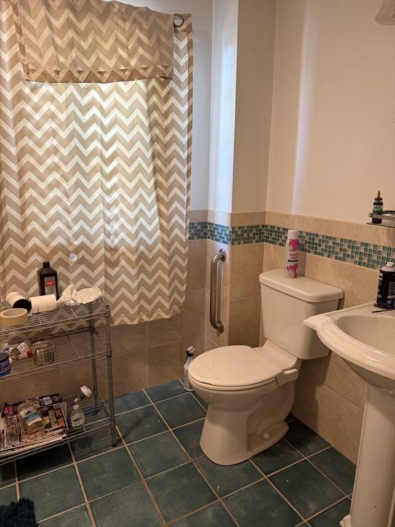 half bathroom featuring tile walls, tile patterned flooring, wainscoting, and toilet