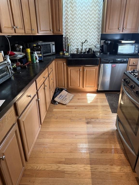kitchen with a sink, dark countertops, stainless steel appliances, and light wood-style flooring