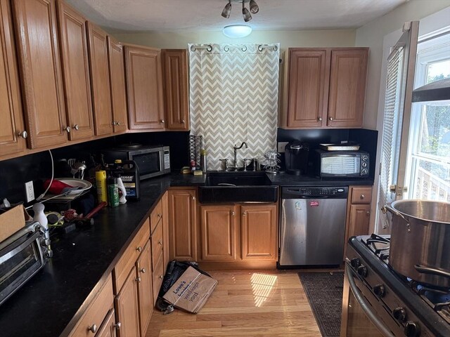 kitchen with appliances with stainless steel finishes, tasteful backsplash, dark countertops, a sink, and light wood-style flooring