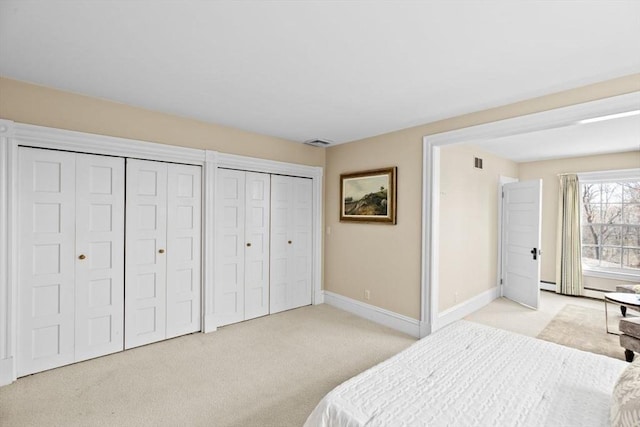 bedroom with baseboards, visible vents, light colored carpet, and two closets