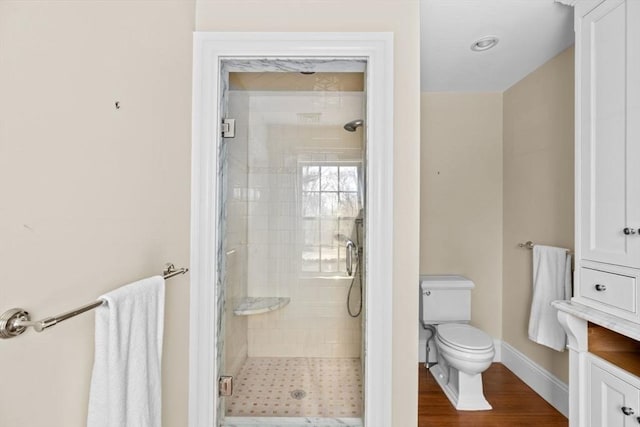 bathroom featuring a shower stall, baseboards, toilet, and wood finished floors