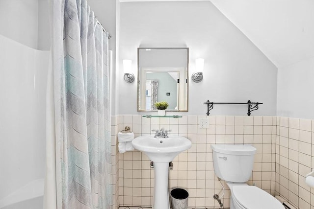 full bathroom featuring vaulted ceiling, a shower with curtain, toilet, wainscoting, and tile walls