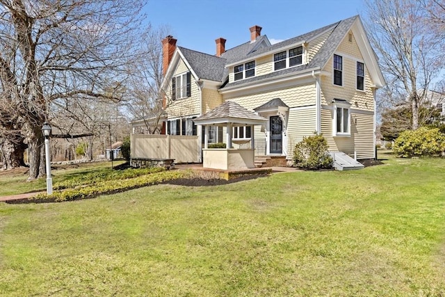back of property featuring entry steps, a lawn, and a chimney
