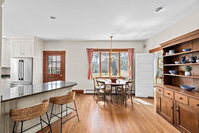 kitchen with dark stone countertops, light wood-style floors, high quality fridge, and a kitchen breakfast bar