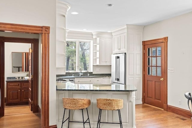 kitchen with a peninsula, light wood-type flooring, open shelves, a sink, and high end fridge