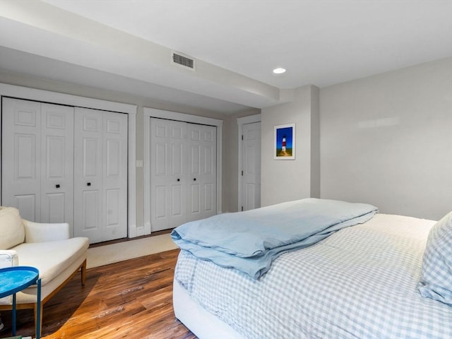 bedroom with two closets, wood finished floors, and recessed lighting