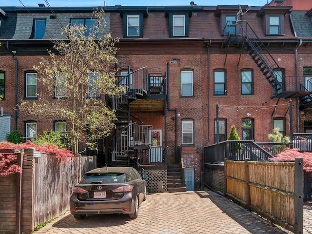 back of property featuring mansard roof, stairway, brick siding, and fence