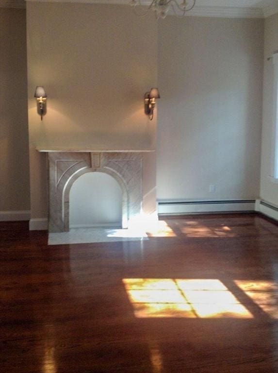 unfurnished living room featuring wood finished floors, baseboard heating, ornamental molding, and baseboards