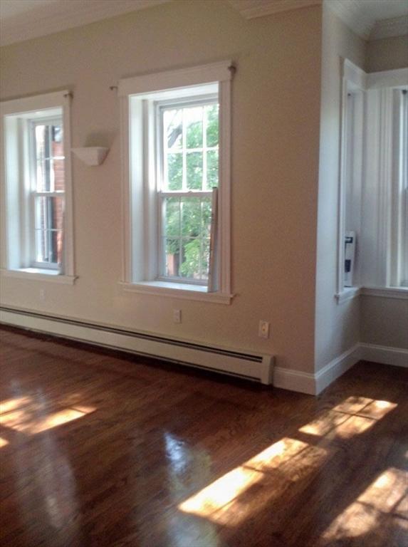 empty room featuring a baseboard radiator, ornamental molding, wood finished floors, and healthy amount of natural light