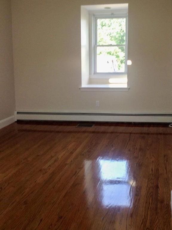 unfurnished room with wood finished floors, baseboards, and a baseboard heating unit