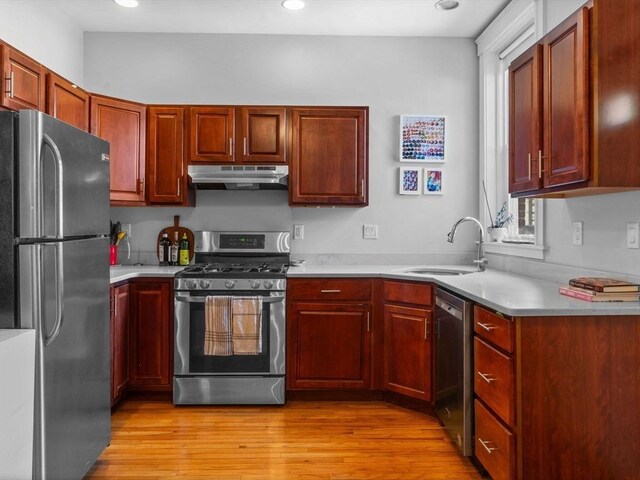 kitchen with stainless steel appliances, a sink, under cabinet range hood, light countertops, and light wood-type flooring