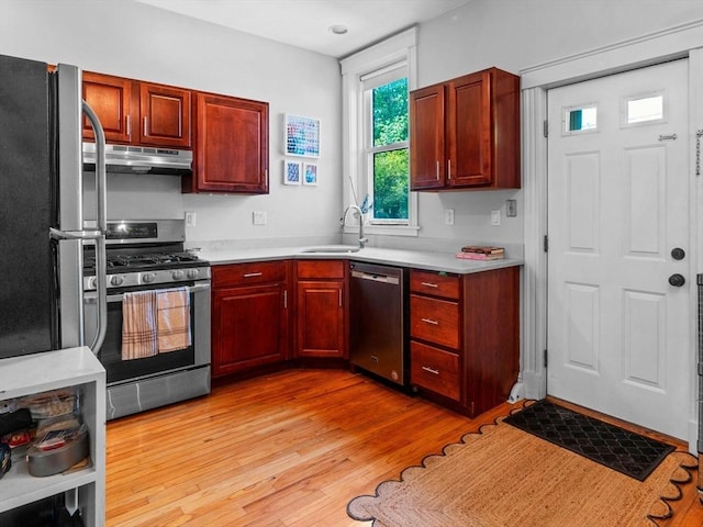 kitchen with appliances with stainless steel finishes, under cabinet range hood, a sink, light wood finished floors, and light countertops
