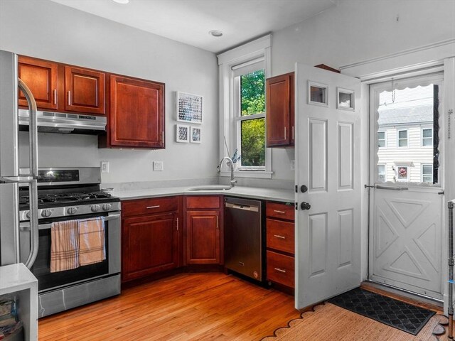 kitchen with appliances with stainless steel finishes, under cabinet range hood, a sink, light wood-style flooring, and light countertops