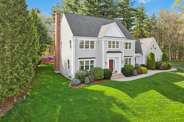 view of front of property featuring roof with shingles, a chimney, and a front lawn