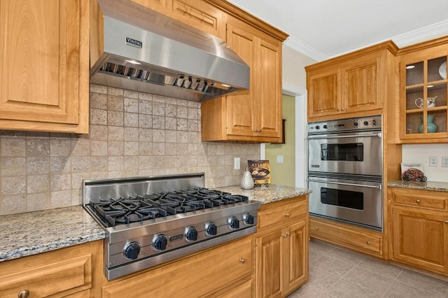 kitchen featuring ornamental molding, light stone countertops, glass insert cabinets, ventilation hood, and stainless steel appliances