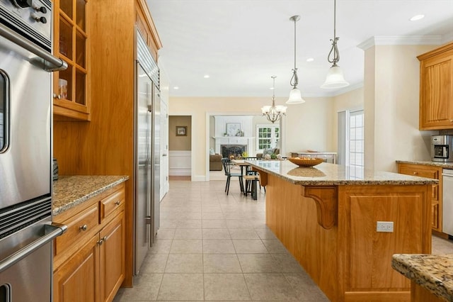 kitchen featuring a kitchen island, light stone countertops, brown cabinets, ornamental molding, and stainless steel appliances