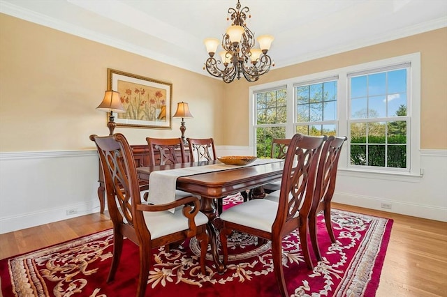 dining area with crown molding, a wainscoted wall, wood finished floors, and a notable chandelier