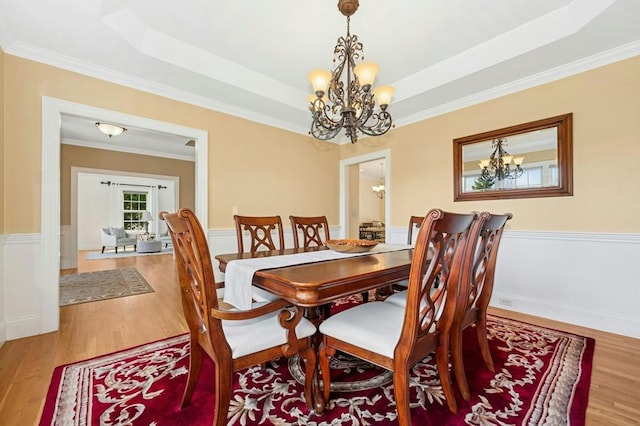 dining area featuring a notable chandelier, a raised ceiling, a wainscoted wall, wood finished floors, and ornamental molding