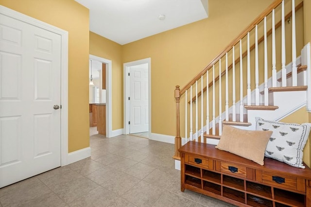 tiled entryway with baseboards and stairs