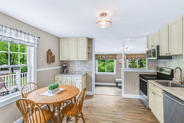 kitchen featuring appliances with stainless steel finishes, a sink, cream cabinets, light wood-style flooring, and backsplash