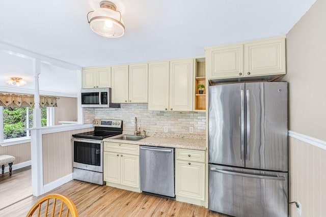 kitchen with stainless steel appliances, a sink, cream cabinets, and light wood-type flooring