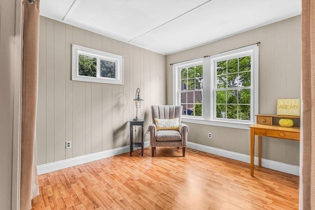 sitting room featuring wood finished floors, plenty of natural light, baseboards, and wooden walls