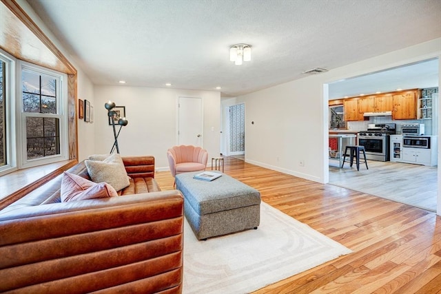 living room featuring light wood finished floors, visible vents, baseboards, a toaster, and recessed lighting