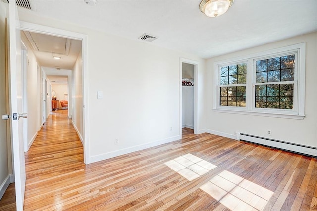 spare room with visible vents, baseboards, attic access, light wood-style floors, and a baseboard heating unit