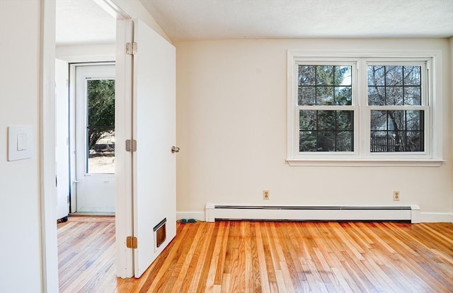 empty room featuring a baseboard radiator, baseboards, and hardwood / wood-style floors