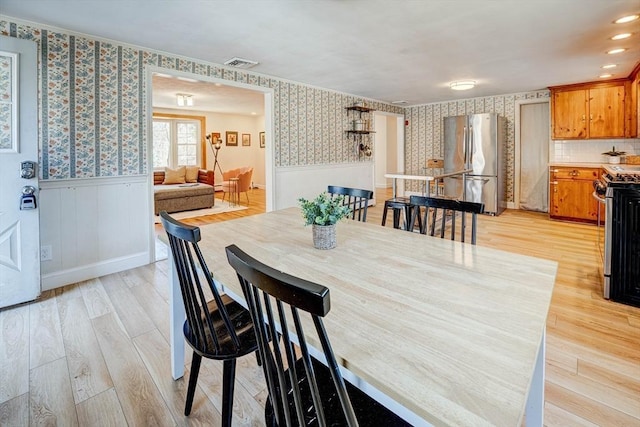 dining area featuring light wood finished floors, visible vents, wainscoting, and wallpapered walls