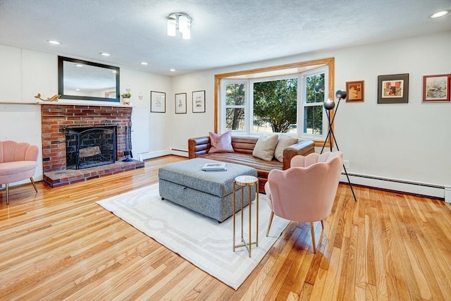 living area featuring a brick fireplace, wood finished floors, a textured ceiling, and a baseboard radiator