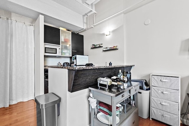 kitchen with dark stone counters, a peninsula, white microwave, and wood finished floors