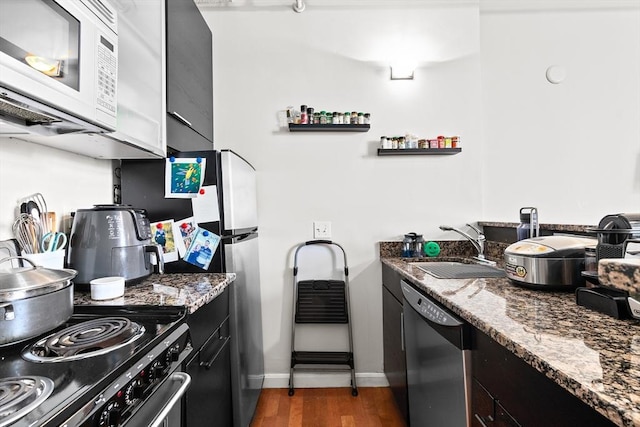 kitchen with dark cabinetry, dark wood finished floors, dishwashing machine, and white microwave