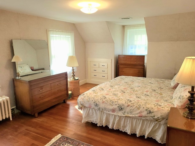 bedroom featuring radiator, multiple windows, vaulted ceiling, and hardwood / wood-style flooring