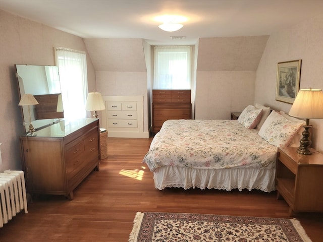 bedroom with wood-type flooring, vaulted ceiling, and radiator