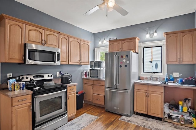 kitchen featuring a ceiling fan, wood finished floors, light countertops, a sink, and stainless steel appliances