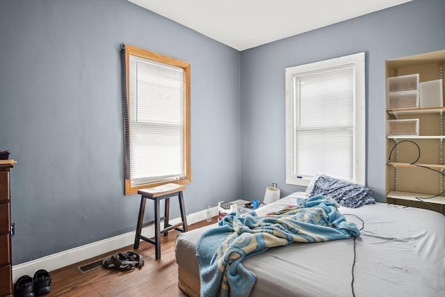 bedroom featuring baseboards, wood finished floors, and visible vents
