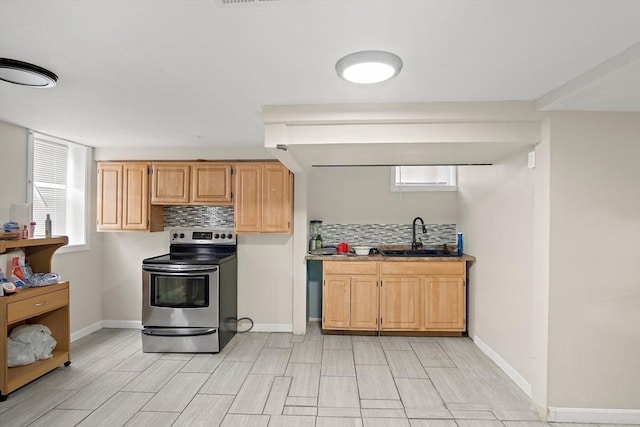 kitchen with a sink, light wood finished floors, stainless steel range with electric stovetop, baseboards, and backsplash