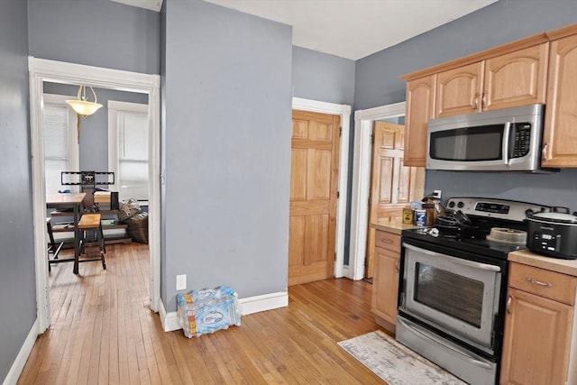 kitchen featuring light wood-type flooring, baseboards, appliances with stainless steel finishes, and light brown cabinets