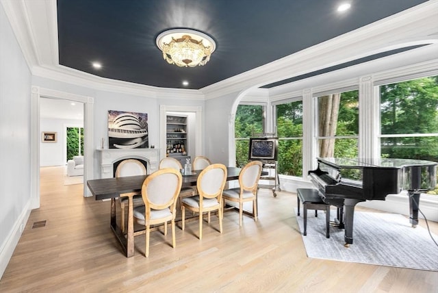 dining area featuring baseboards, a raised ceiling, light wood-style flooring, and ornamental molding