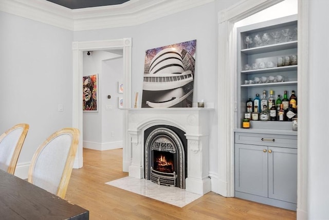 interior space with crown molding, a fireplace with flush hearth, light wood-style floors, and built in features