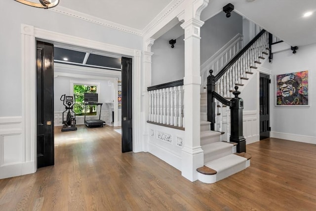 entryway with ornamental molding, stairs, decorative columns, and wood finished floors