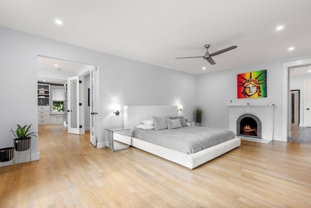 bedroom featuring baseboards, ceiling fan, a fireplace with flush hearth, recessed lighting, and light wood-style floors