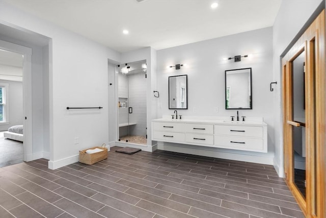ensuite bathroom with a sink, wood finished floors, a shower stall, double vanity, and baseboards