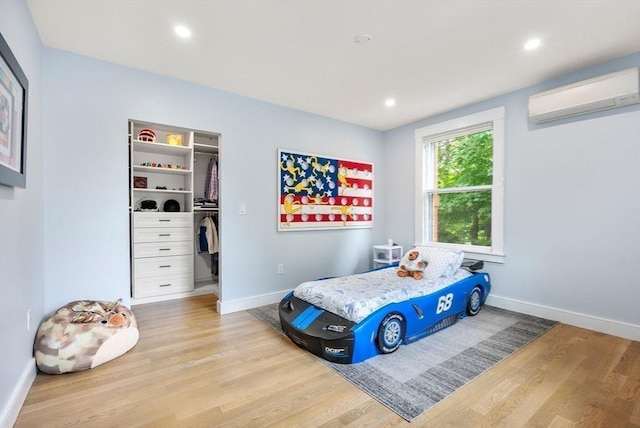 bedroom featuring a wall mounted air conditioner, baseboards, light wood-style floors, and a spacious closet