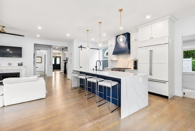 kitchen with paneled refrigerator, light wood-type flooring, open floor plan, custom exhaust hood, and a large island with sink
