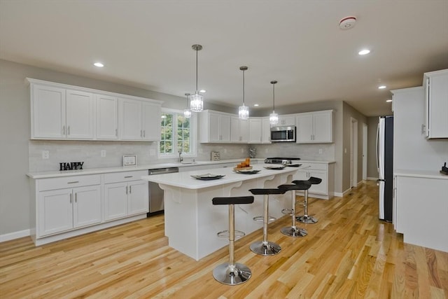 kitchen featuring appliances with stainless steel finishes, a kitchen breakfast bar, a center island, light countertops, and white cabinetry