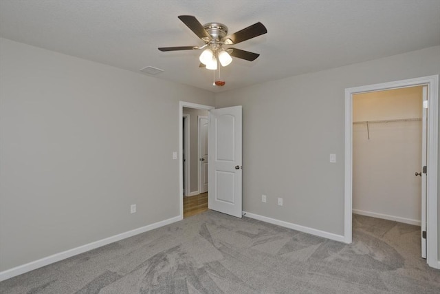 unfurnished bedroom with a spacious closet, carpet floors, a ceiling fan, and baseboards