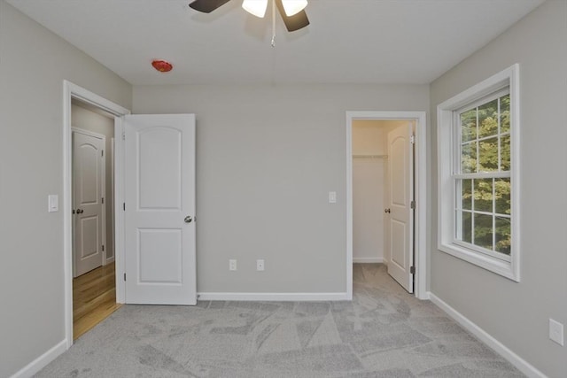 unfurnished bedroom with multiple windows, a walk in closet, and light colored carpet