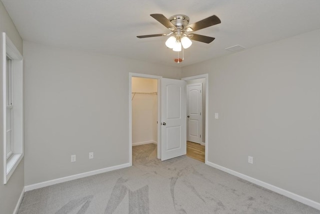 unfurnished bedroom featuring a walk in closet, carpet, a closet, a ceiling fan, and baseboards